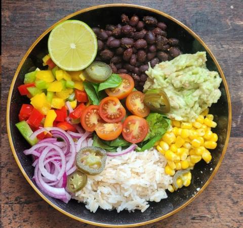 a bowl of food including rice, onions, tomatoes, peppers, beans and a lime